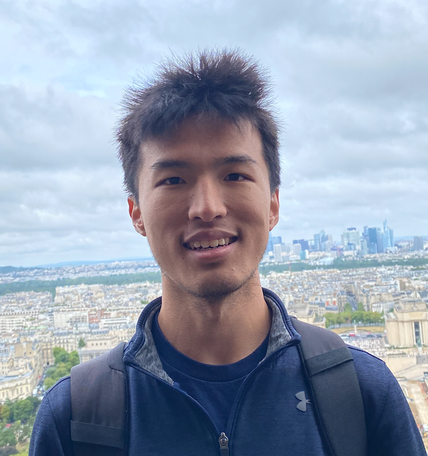 A picture of an Asian-American boy with a blue jacket, standing in front of the Paris skyline.